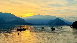 A calm lake with sailboats at sunset, surrounded by mountains. - Affittacamere Piazza (Verbania)
