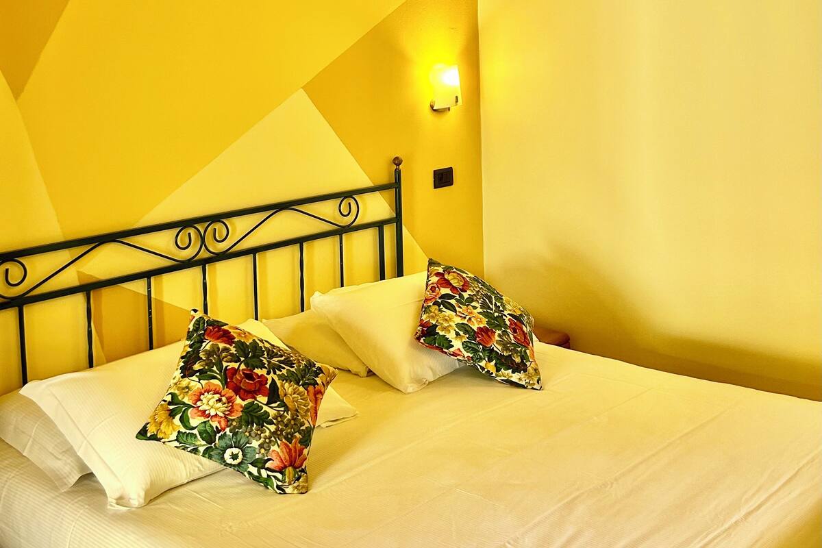 Una habitación con cama, almohadillas florales, diseño geométrico en la pared y techo de madera.