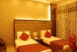 A hotel room with two beds, a wooden headboard, patterned wallpaper, and a curtain with circular designs. - Hotel Yug Villa (New Delhi)