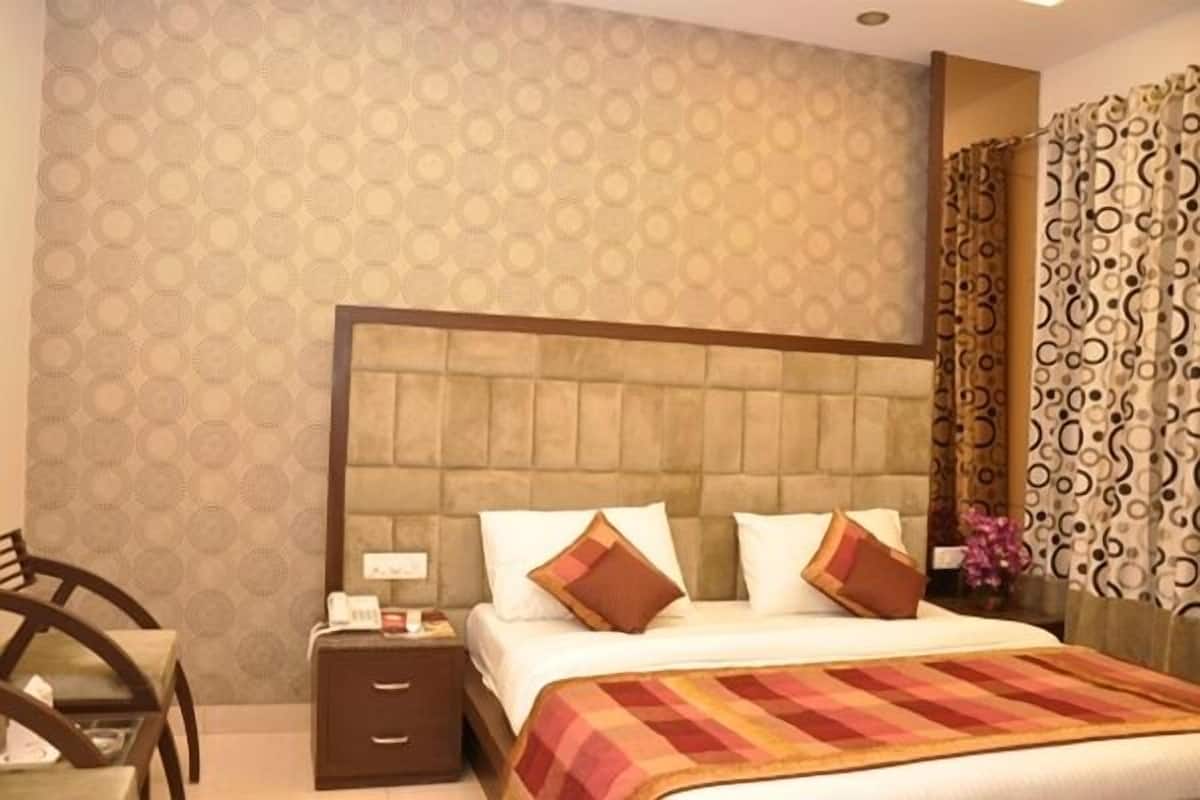 A hotel room with a large bed, a nightstand, a chair, and patterned wallpaper.