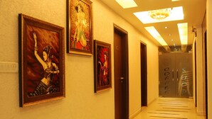 A hallway with framed artwork on the walls, a ceiling light fixture, and a door with 'COFFEE' written on it. - Hotel Yug Villa (New Delhi)