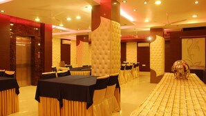 A banquet hall with tables set for events, a large buffet table, and a ceiling fan. - Hotel Yug Villa (New Delhi)