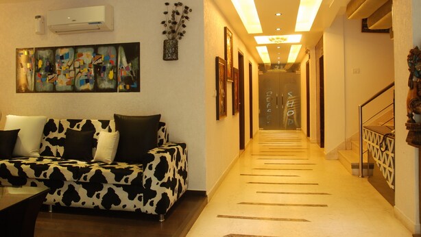 A modern living room with a cow print sofa, a coffee shop sign, and a hallway leading to a staircase. - Hotel Yug Villa (New Delhi)