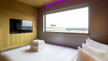 Habitación de hotel con una cama, un televisor fijado a la pared, una ventana con vistas a edificios y una pila de toallas.