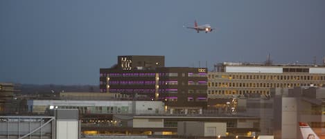 Un aeropuerto con un avión despegando, edificios con letreros iluminados y una zona de terminales con vehículos e infraestructura aeroportuaria.