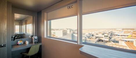 A hotel room with a large window offering a view of the airport and airplanes.