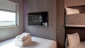 Habitación de hotel moderna con cama, una pila de toallas blancas, televisión integrada y vista al aeropuerto a través de una ventana.
