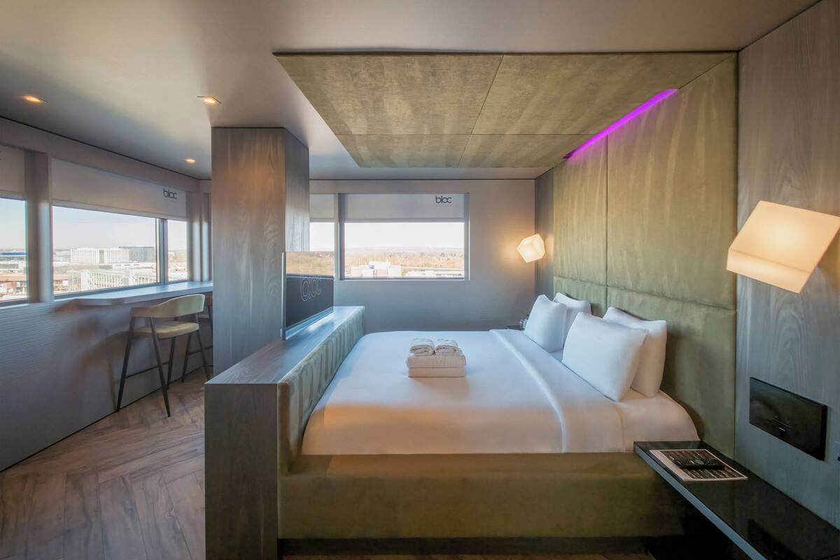 A modern hotel room with a large bed, a desk, and a view of the city.