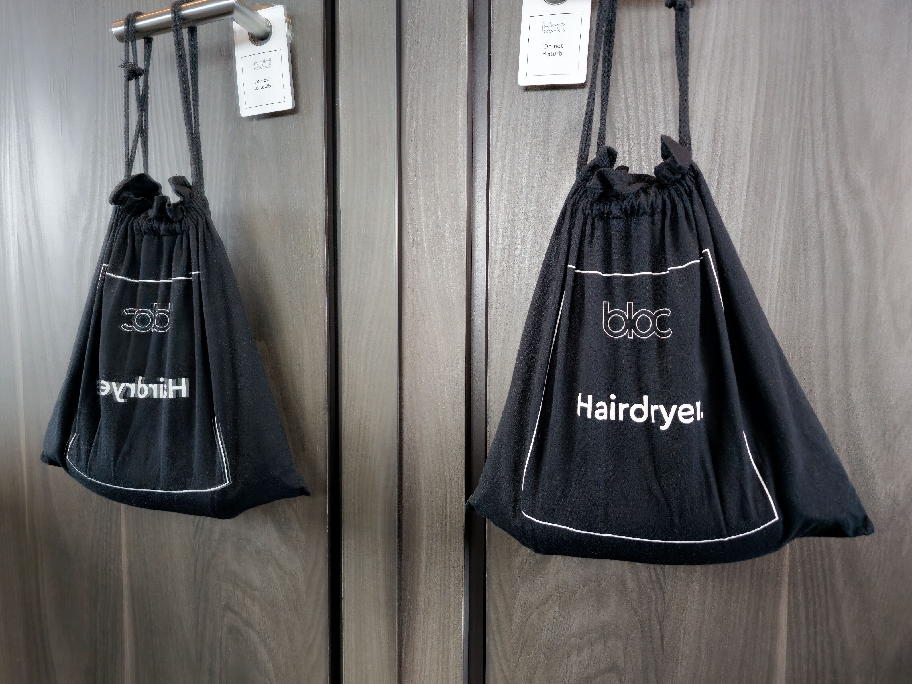 A black hairdryer bag with 'bloc' and 'Hairdryer' text hanging on a door handle.