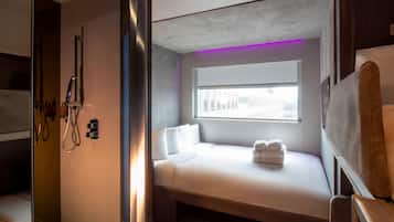 A compact hotel room with a bed, a window, and a shower area.
