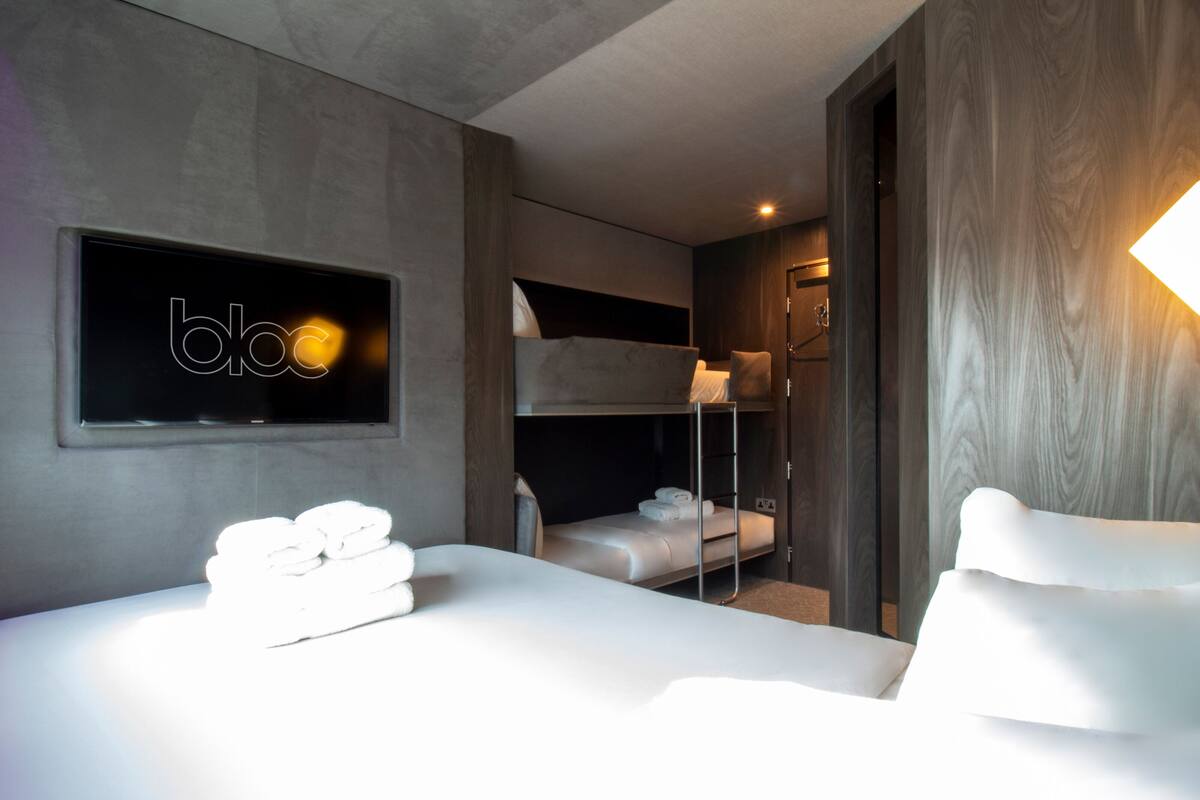 A modern hotel room with a bunk bed, a flat bed, and a wall-mounted TV.