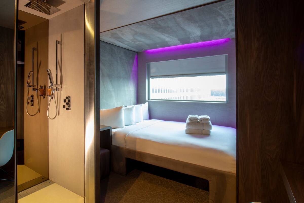A modern hotel room with a bed, a window with a view, and a shower area.