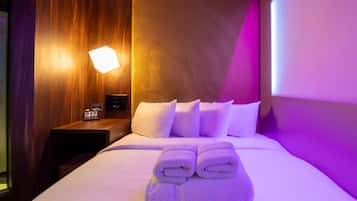 A hotel room with a neatly made bed, a bedside table with a lamp, and a wall-mounted control panel.