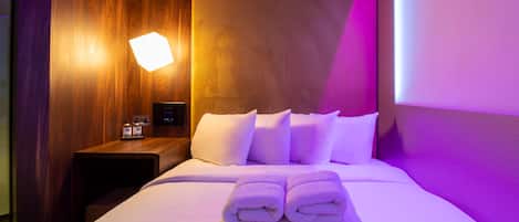 A hotel room with a neatly made bed, a bedside table with a lamp, and a wall-mounted control panel.