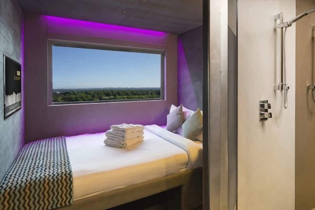 A room with a bed, a window, a shower, and a view of the landscape.