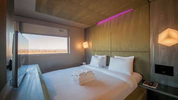 Una habitación de hotel moderna con una cama grande, una mesita de noche, una lámpara de pared y una ventana con vistas.