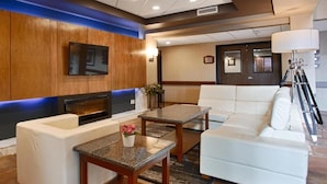 Eine moderne Hotellobby mit einem weißen Sofa, einem kleinen Tisch mit Blumenvase, einem an der Wand befestigten Flachbildfernseher und einem Kamin.