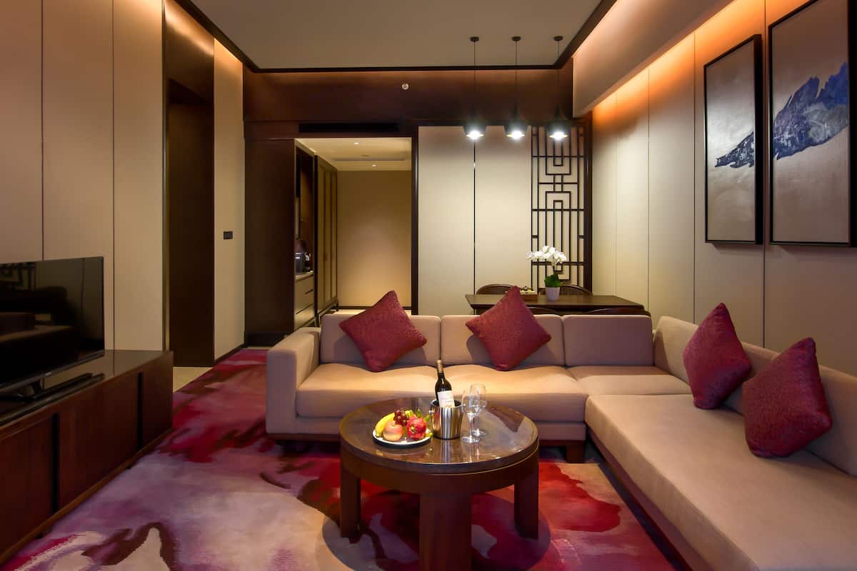A modern living room with a sofa, a TV, a dining table with a vase of flowers, and a red carpet.
