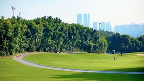 Un campo de golf con un camino sinuoso, césped verde exuberante y altos edificios al fondo.