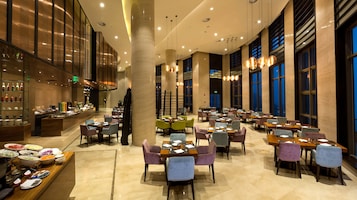Un amplio vestíbulo de hotel con varias zonas de restauración, un bar y un bufé con diversas opciones de comida.