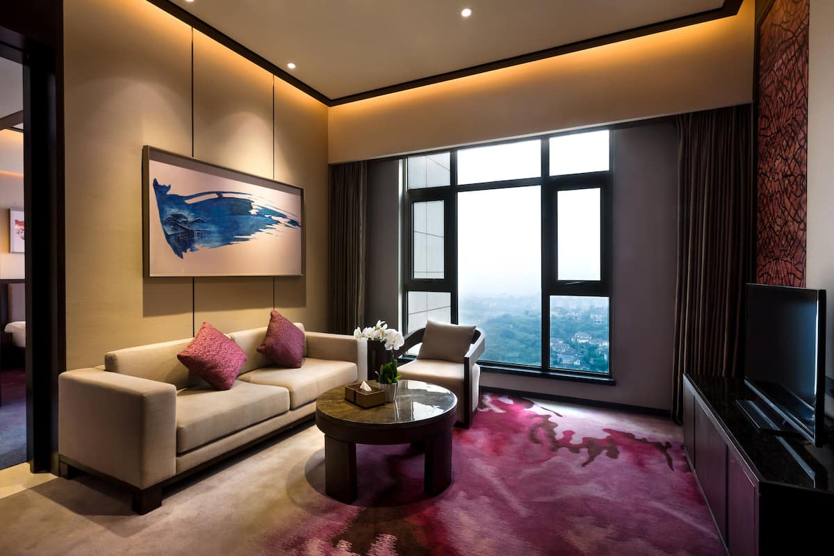 A modern living room with a sofa, armchair, coffee table, and a large window offering a city view.