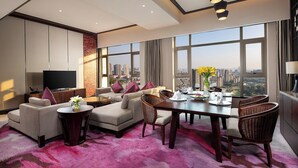 A modern living room with a sofa set, a dining table with chairs, a TV, and a large window with a city view. - Crowne Plaza Chongqing New North Zone by IHG (Chongqing)