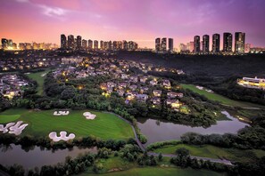 A residential area with houses, a golf course, and a city skyline in the background. - Crowne Plaza Chongqing New North Zone by IHG (Chongqing)