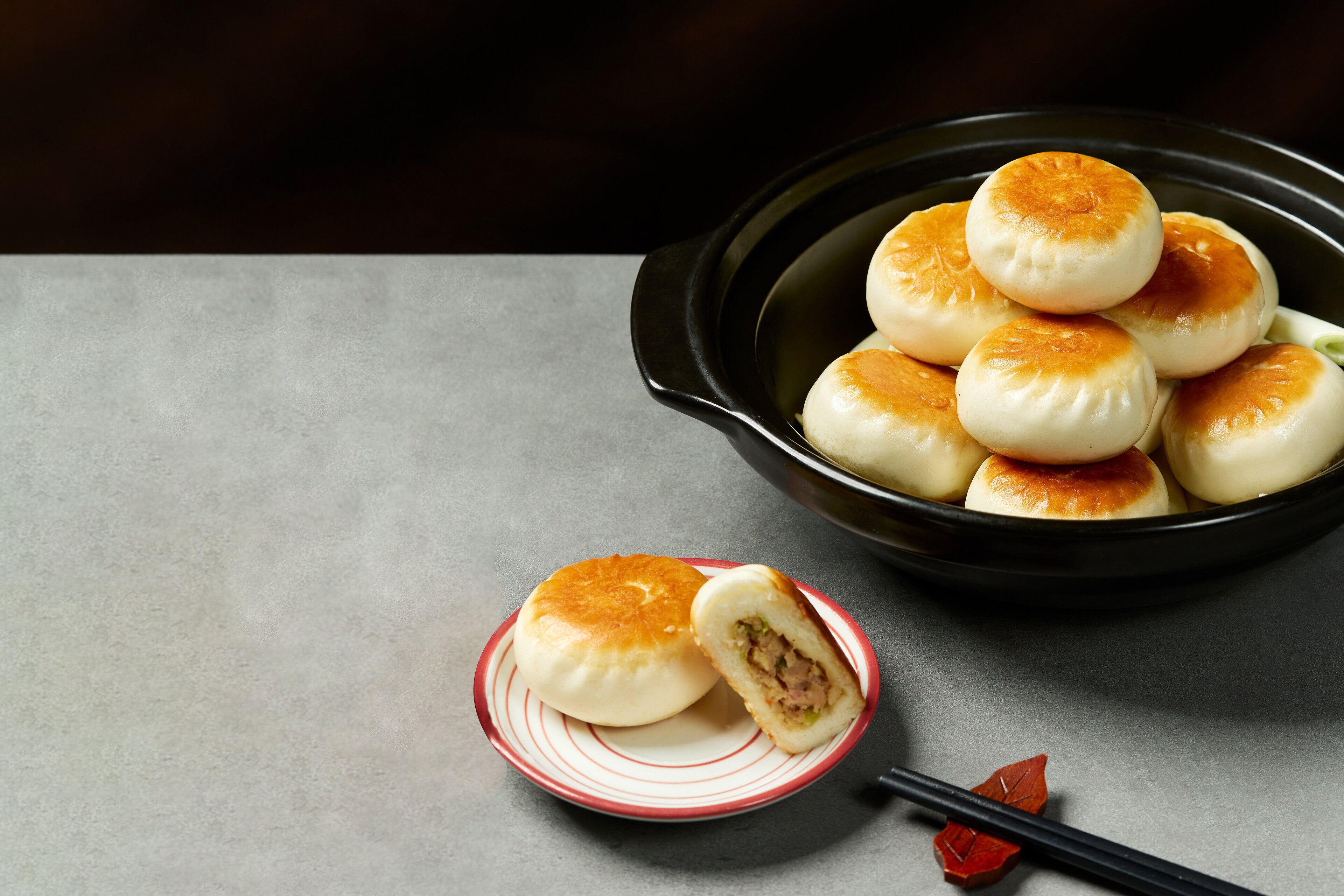 A bowl of steamed buns on a plate with a pair of chopsticks beside it.