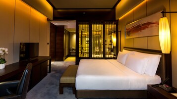Habitación de hotel con cama, mesita de noche, televisor, escritorio y baño visible mediante una separación.
