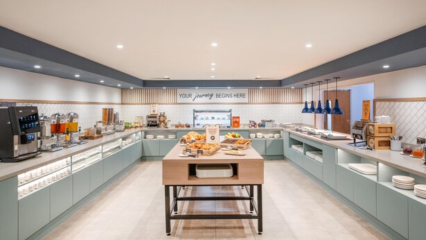 A modern breakfast buffet with a central serving table, a coffee station, and a sign that reads 'YOUR journey begins here.' - Hampton By Hilton Sheffield (Sheffield)