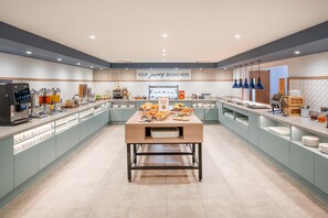 Un buffet de desayuno moderno con una mesa central de servicio, una estación de café y un letrero que dice 'YOUR journey begins here'.