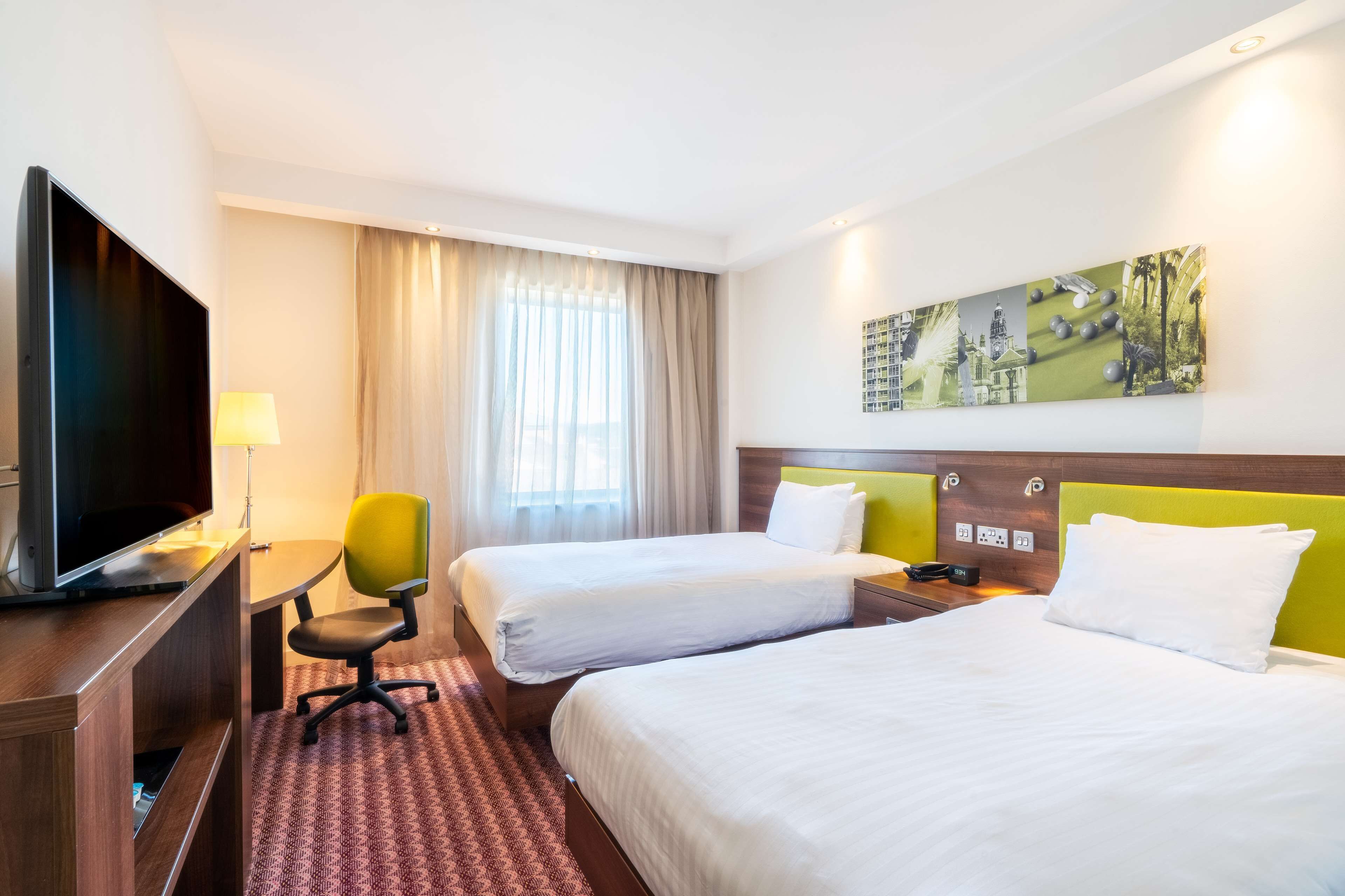 A hotel room with two beds, a TV, a desk, and a painting on the wall.
