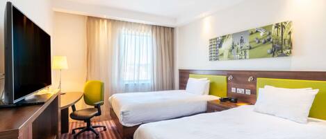 A hotel room with two beds, a TV, a desk, and a painting on the wall.