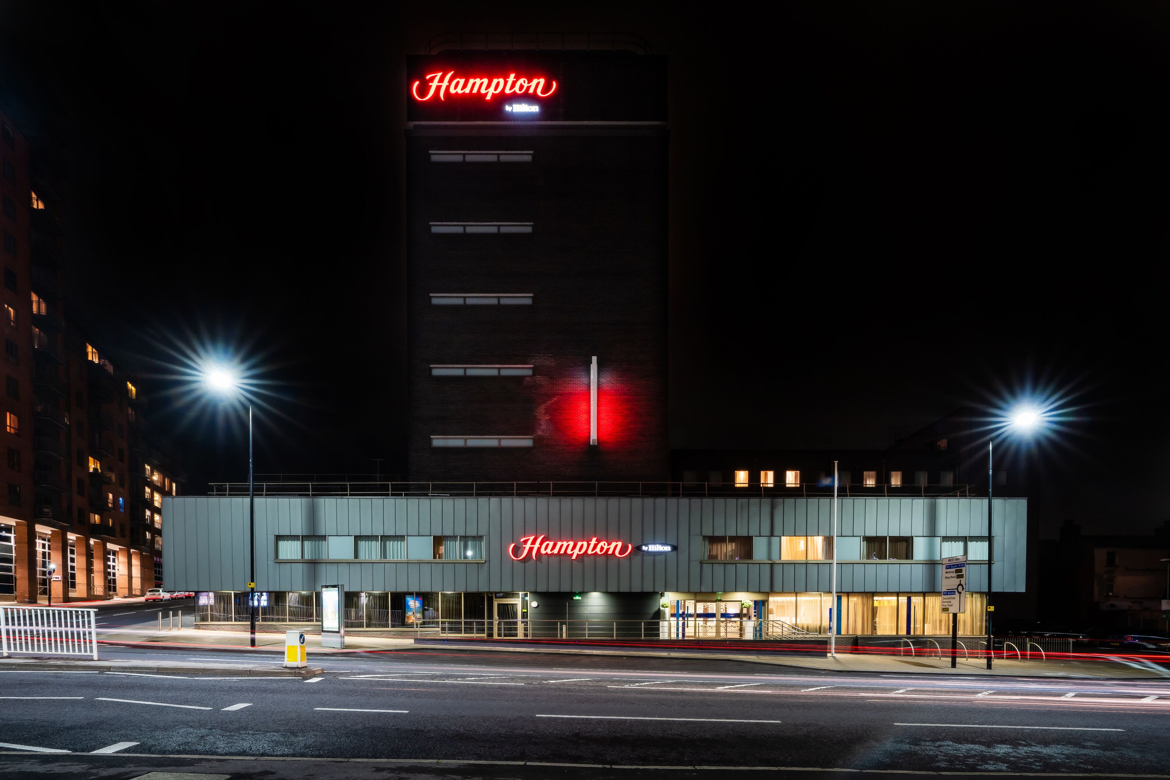 A building with a prominent 'Hampton' sign, featuring a modern architectural style with a flat roof and a series of windows.