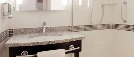 Un baño moderno con lavamanos de granito, un espejo, cabina de ducha de vidrio y una toalla blanca en el suelo.