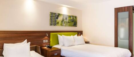 A hotel room with two beds, a green headboard, and a painting on the wall.