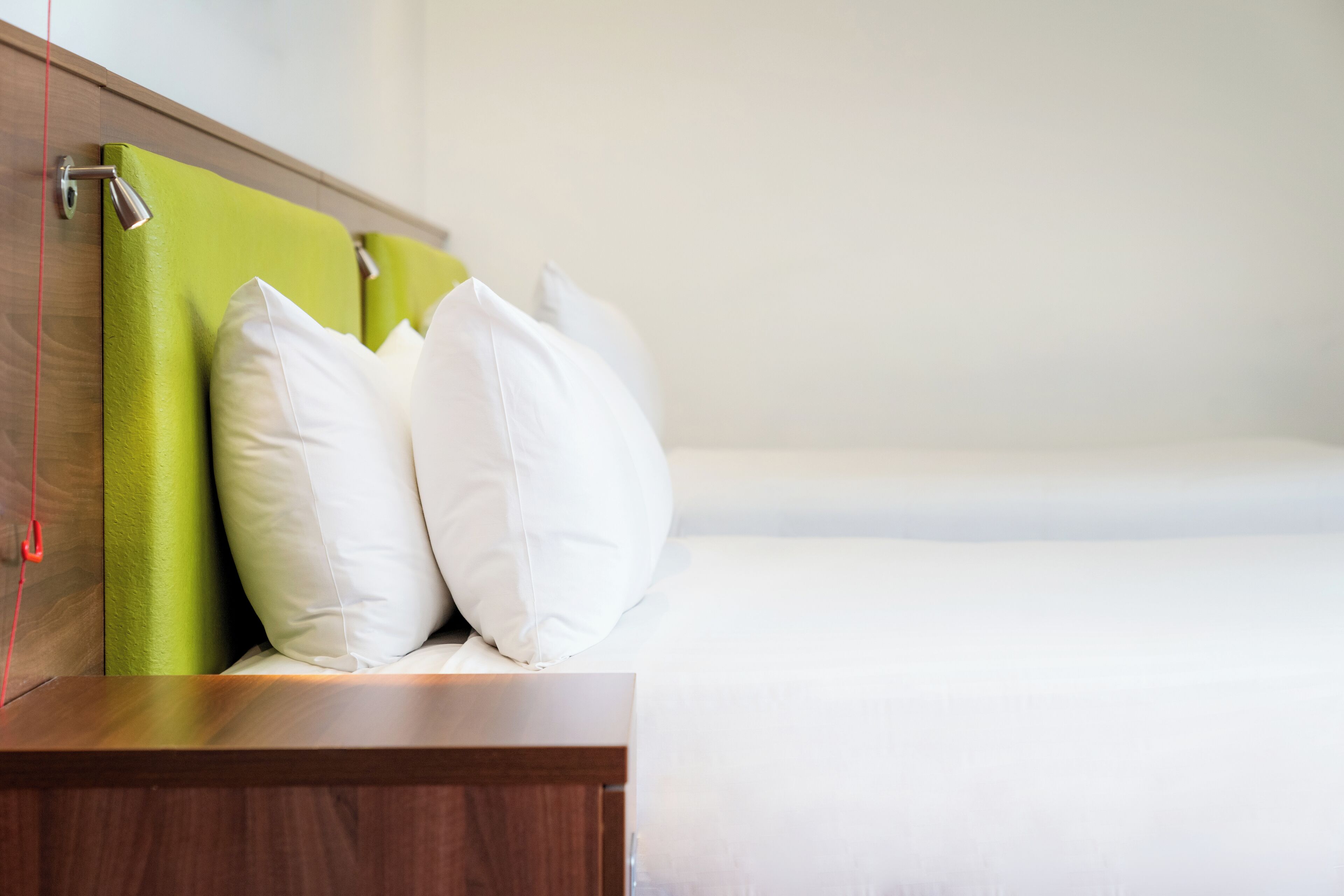 A neatly made bed with white bedding and a green headboard.