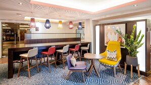 A modern hotel lobby with a central bar area, multiple seating options including bar stools and chairs, and a large potted plant. - Hampton By Hilton Sheffield (Sheffield)