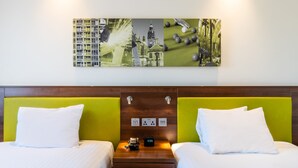 A hotel room with two beds, a wooden headboard, a wall-mounted artwork, and a nightstand with a clock and electrical outlets. - Hampton By Hilton Sheffield (Sheffield)