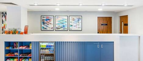 A reception area with a counter, snack dispensers, a refrigerator, and a blue storage cabinet.