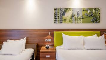 Ein Hotelzimmer mit zwei Betten, einem grünen Kopfteil, einem Nachttisch mit Telefon und Lampe sowie einem an der Wand hängenden Kunstwerk.