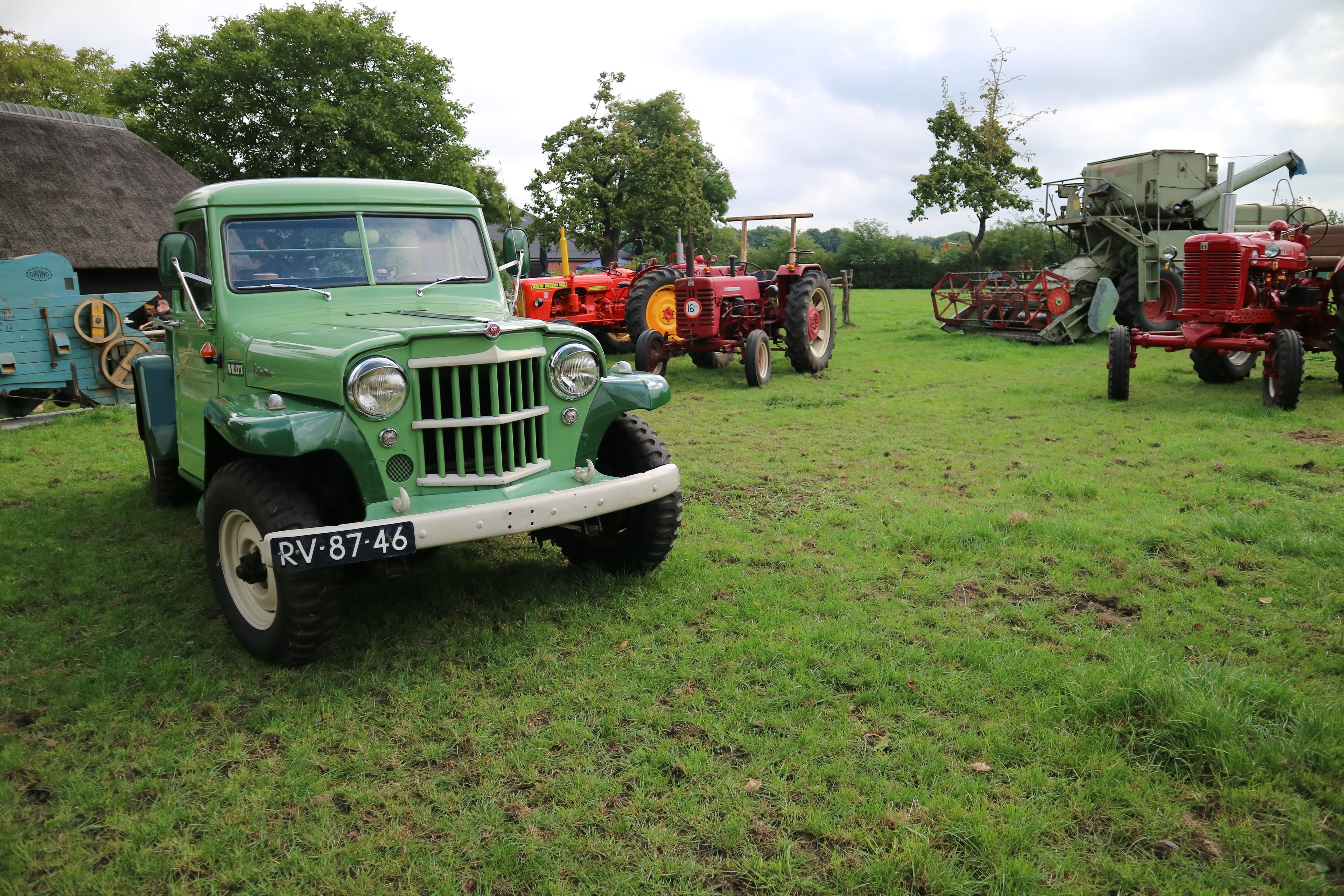A green vintage car with a license plate RV-87-46 parked in a grassy field.