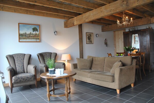 A living room with a wooden ceiling, a sofa, two armchairs, a round table with a lamp, and a painting on the wall. - Den Heijkant (Moergestel)