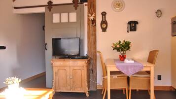 A dining area with a wooden table, wicker chairs, a television on a wooden cabinet, and a wall clock.