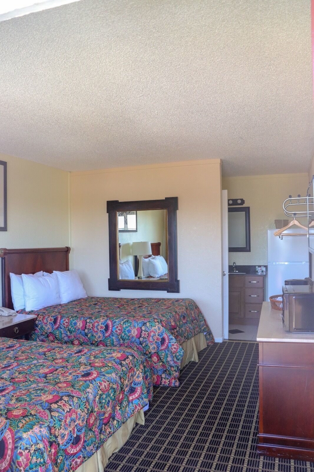 A hotel room with a large bed, a dresser, a mirror, and a kitchenette area.