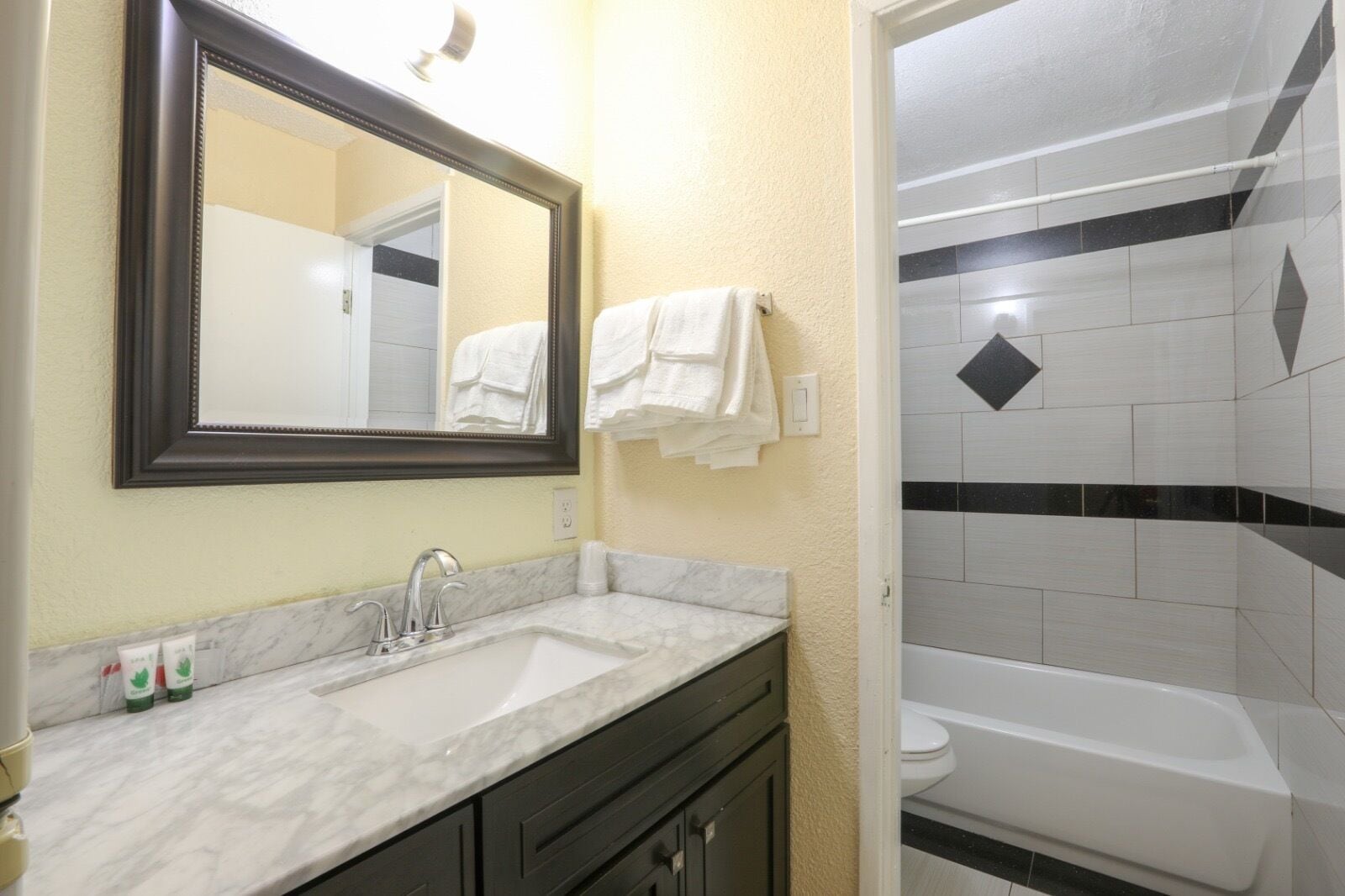 A bathroom with a marble sink, a large mirror, a white bathtub, and black and white tiles.