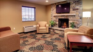A living room with a stone fireplace, a flat-screen TV, and a patterned carpet. - Cobblestone Hotel & Suites - Newton (Newton)