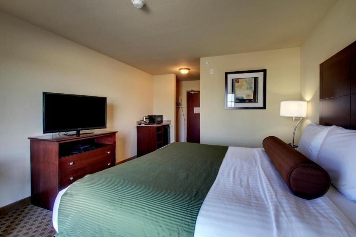 A hotel room with a bed, a television, a desk, and a lamp.