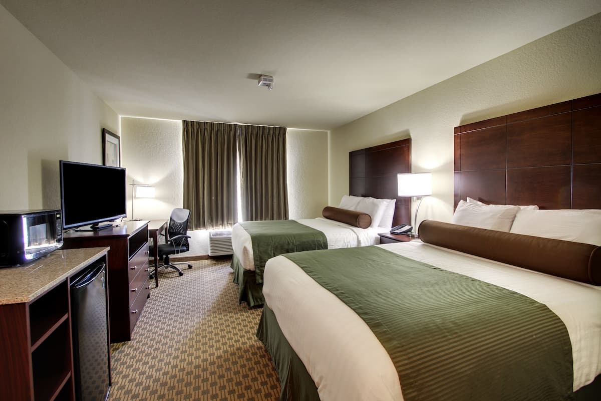 A hotel room with two beds, a desk with a television, a chair, a lamp, and a window with curtains.