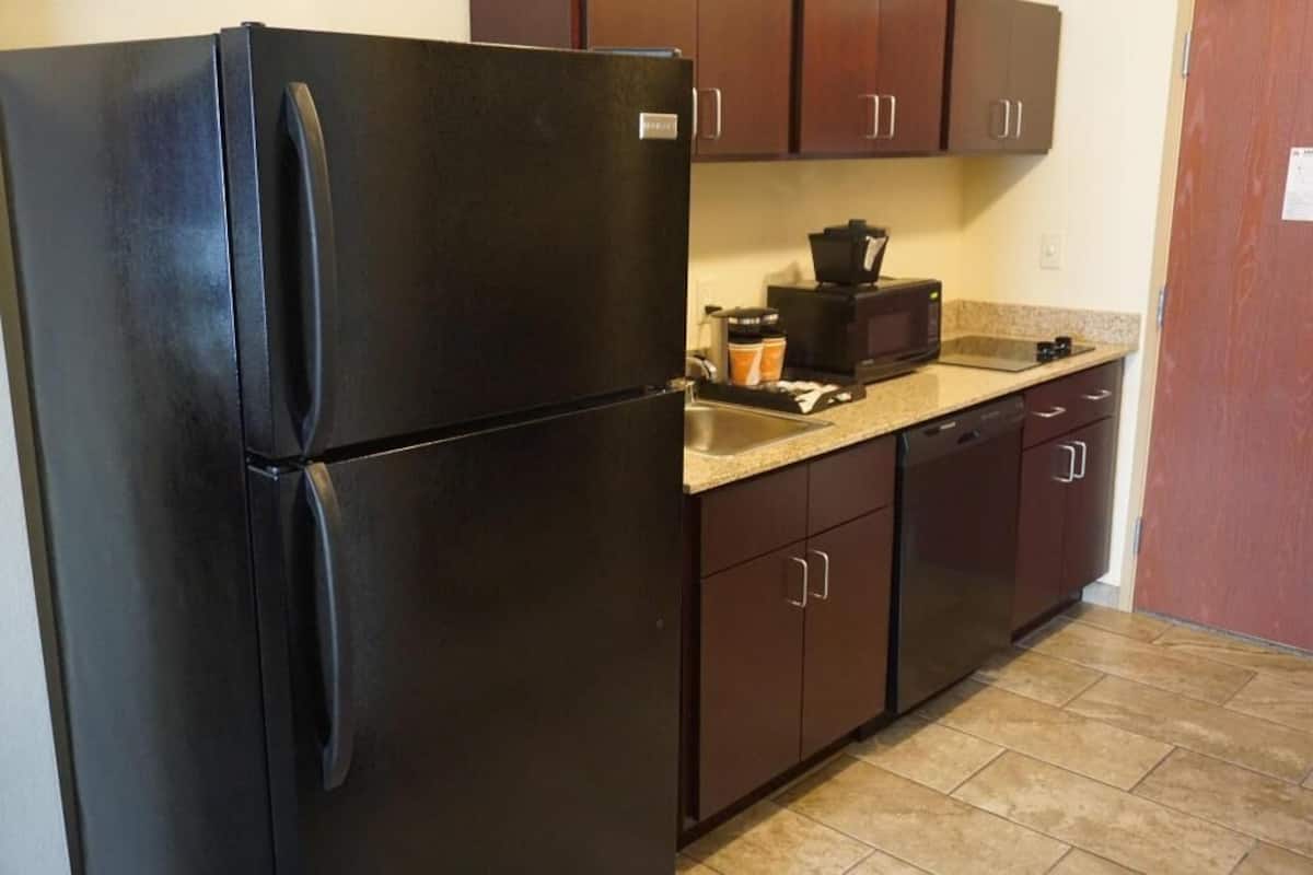 A kitchen with a black refrigerator, dark brown cabinets, a countertop, and a sink.